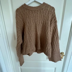 Beige stickad tröja från Gina Tricot - Säljer en beige stickad tröja från Gina Tricot i storlek XS. Tröjan har ett snyggt kabelstickat mönster, ribbade muddar och rund hals. Perfekt för dig som gillar en chill och cozy vibe under hösten och vintern.