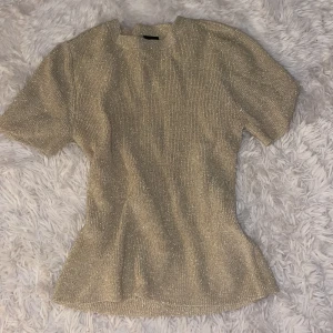 Topp Gina - Supersnygg glittrig topp i guld från Gina Tricot. Perfekt för att sticka ut och ge din outfit extra bling. Använd en gång 