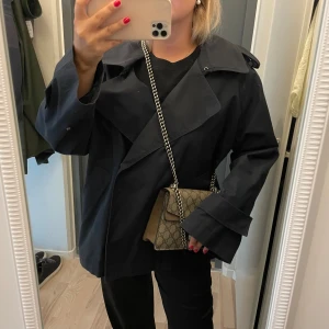 Svart trenchcoat med bred krage - Marinblå trenchcoat från Massimo Dutti med bred krage och oversized passform. Jackan har långa ärmar med extra breda muddar och snygga detaljer på axlarna.