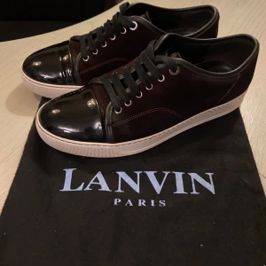Lanvin sneakers  - Unika Lanvins i en exklusiv färgkombination som inte längre tillverkas – vinröd mocka kombinerat med svart lackad tå, röda sömmar och svarta snören. Passar perfekt för dig som har runt storlek 43 och söker något som verkligen sticker ut. Skorna har använts mycket sparsamt och är i fint skick. Ny mockaborste och original påse medföljer.