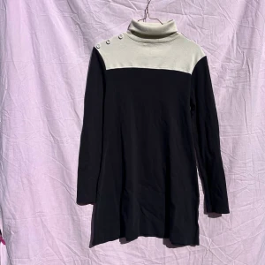 Svart och vit poloklänning River Island - Snygg kortklänning från River Island med svart kropp och vit överdel. Klänningen har polokrage, långa ärmar och dekorativa knappar på axeln. Tillverkad i mjuk bomull med lite stretch i ärmarna för extra komfort. Perfekt för dig som gillar stilren design.