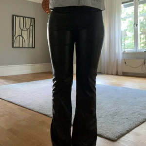 Svarta bootcut byxor i skinnimitation - Säljer ett par svarta byxor i skinnimitation med bootcut-modell. Sitter perfekt i längden på mig som är 168.