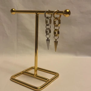 Chunky örhängen med kedjor och spikes - Säljer ett par statement örhängen med kedjelänkar i både silver och guld. Örhängena har coola konformade spikes som hänger längst ner och små glittriga stenar på ringarna. Perfekt för dig som gillar edgy och trendiga accessoarer.
