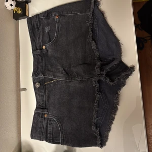 Svarta jeansshorts från H&M Divided - svarta jeansshorts från H&M Divided med råå fransiga kanter, dragkedja och knapp framtill samt slitna detaljer på fickorna. Sist jag använde dem var ett bra tag sen. Säljer då de inte passar mig längre. De är i storlek 42. Står ej för postens slarv.
