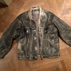 Svart skinnjacka från Mustang - Riktigt cool svart skinnjacka från Mustang med klassisk jeansjacke-look. Jackan har två bröstfickor med knappar, markerade sömmar och en snygg krage. Materialet är äkta skinn med en mörk, lite sliten finish som ger jackan extra karaktär. Bara använt en gång, så bra skick🩷🩷🩷 köpt för 2500kr