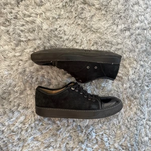 Lanvin Svarta sneakers med lackad tå  - Säljer ett par svarta sneakers med snygg snörning och rund tå i blankt lackmaterial. Skorna har ovandel i mocka och insida i skinn, vilket gör dem både bekväma och stilrena. Metallöglor vid snörningen ger en cool touch. Perfekt för dig som gillar minimalistisk design.