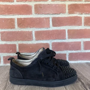 Christian Louboutin  - Säljer ett par svarta loubs i mocka med platt. Skorna har snörning och är dekorerade med svarta nitar över hela tån för en edgy vibe. Perfekta för dig som vill sticka ut med din stil och gillar detaljer som syns.