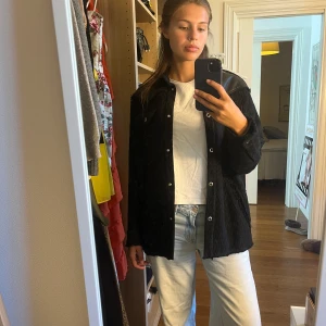 Svart overshirt från IRO med skinn - Skit snygg svart vår/höstjacka från IRO med coola skinnpaneler över axlarna och kragen. Jackan har ett grovt stickat mönster, tryckknappar framtill och två bröstfickor. Hittar inte exakta nypriset då den inte säljs längre. Men liknande jackor från märket kostar mellan 5000-10000 kr. 