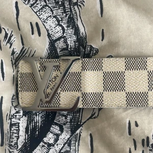 L bälte - Snyggt skärp  med klassiskt rutigt mönster i beige och grått. Bältet har ett stort, silverfärgat spänne framtill och är gjort i skinn. Lite använt också priset diskuteras.