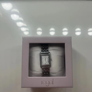 Regal rektangulär silverfärgad klocka - Stilren klocka från Regal med rektangulärt ur och klassisk länkarmband i silverfärgat metall. Vit urtavla med svarta romerska siffror och diskret logga. Perfekt för dig som gillar en clean och tidlös look. Lätt att matcha med olika outfits.