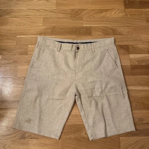 Beige linne-shorts från Burberry - Snygga beige shorts från Burberry i linne med klassisk passform och midwaist. De har diskret Burberry-logga broderad på benet, sidofickor och bakfickor med knapp. Perfekta för varma sommardagar och har en stilren look med bälteshällor och knappstängning.