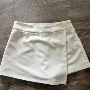 Vita omlottshorts från Forever21 - Snygga vita omlottshorts från Forever21 med stilren design och bred linning. Shortsen har en omlott-detalj framtill som ger en kjol-look och är tillverkade i ett mjukt syntetmaterial. Perfekta för varma dagar och passar dig som gillar minimalistisk stil.