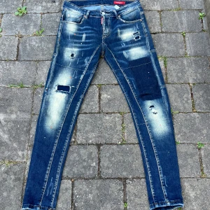 Dsquared2 skinny jeans med slitningar - Säljer ett par blå skinny jeans från Dsquared2 med coola slitningar, patchade detaljer och blekta partier. Jeansen har klassisk femficksdesign, låg midja och snygga kontrastsömmar. Materialet är jeans med stretch för skön passform. Perfekt för dig som gillar streetstyle.