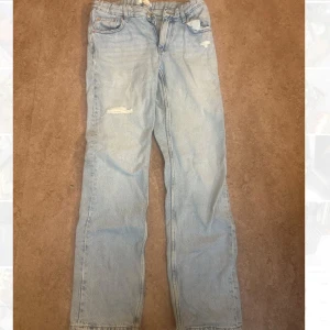 Ljusblå raka jeans med slitningar - Säljer ett par ljusblå jeans med raka ben och coola slitningar på låret och fickan. Klassisk femficksmodell med knapp och dragkedja framtill. Perfekt för dig som gillar en avslappnad och trendig stil.