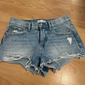 Blå jeansshorts från Gina tricot - Snygga blå jeansshorts från Gina tricots kollektion ”Perfect Jeans” med  fransade kanter. De har slitna detaljer framtill och klassisk femficksdesign. Materialet är robust denim och shortsen har knapp och dragkedja i gylfen. Perfekt för en chill sommarlook. Säljer då de tyvärr blivit för små för mig!