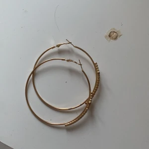 Guldiga hoops med kors och stenar - Stora, runda örhängen i guldton med glittrande stenar som bildar ett kors på varje öron hänge 