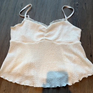 Vit linnetopp med spets från SHEIN - Säljer en vit linnetopp från SHEIN i storlek M. Toppen har tunna axelband, söt spetskant vid halsen och ett smockat, lätt vågigt tyg som ger en chill vibe. Perfekt för varma dagar och enkel att styla med jeans eller kjol.