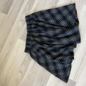Svart rutig kortkjol med volang - Säljer en svart kortkjol med vitt rutmönster och volangig nederkant. Är i storlek M men passar även S.  Kjolen har en bred resår i midjan som gör den enkel att dra på och ger en skön passform. Perfekt för dig som gillar en edgy och chill stil.