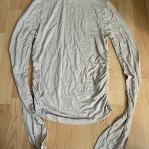 Beige långärmad topp med rynkade sidor - Säljer en beige långärmad topp med snygga rynkade detaljer längs sidorna. Modellen är figurnära och har en mjuk känsla, perfekt för att styla med jeans eller kjol. Materialet känns lätt och stretchigt, vilket gör den skön att bära hela dagen.