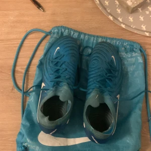 Nike blå fotbollsskor med snörning - Säljer ett par blå Nike Phantoms fotbollsskor Skorna har snörning och en mönstrad ovandel i syntetmaterial för extra grepp. . Dom är använd en gång på match och tre träningar 