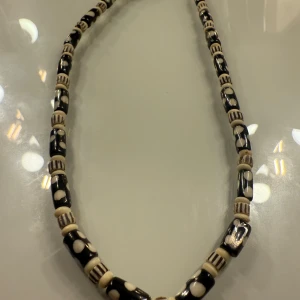 Svart och vit pärlhalsband med prickar - Unikt halsband med svarta och vita pärlor i cylinderform, dekorerade med prickigt och randigt mönster. Pärlorna är varvade och ger ett coolt, retro vibe. Halsbandet har ett metallspänne som gör det enkelt att ta av och på. Perfekt för dig som gillar att sticka ut.