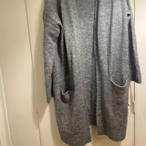 Grå stickad kofta med fickor S  - Mysig grå stickad kofta från SIS i storlek S. Koftan har lång ärm, två stora fickor framtill och ribbade muddar vid ärmslut och nederkant. Perfekt att slänga på sig när det är kyligt ute. Enkel och clean look som funkar till jeans eller leggings.