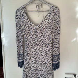 Vit blommig kortklänning Hollister - Supersöt vit kortklänning från Hollister med blått och lila blommönster. Klänningen har långärmade ärmar med snygga detaljer och smock i ryggen. V-ringad hals och knytband i nacken ger en chill vibe. Perfekt för vår och sommar!