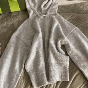 Grå hoodie med huva och ribbad kant - Mysig grå hoodie med huva och bred ribbad kant vid midjan och ärmsluten. Tröjan har lång ärm och en loose passform, perfekt för chill dagar. Materialet känns mjukt och skönt mot huden. Enkel och stilren design som funkar till det mesta.