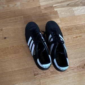 Adidas Copa Mundial fotbollsskor 39⅓ - Adidas Copa Mundial fotbollsskor i svart och vitt med klassiska tre ränder på sidan. Skorna har snörning, rund tå och platt sula med dobbar för gräsplan. Tillverkade i skinn för grym komfort och känsla på planen. Perfekta för dig som vill ha retrostil och kvalitet.Perfekt skick näst intill oanvända.