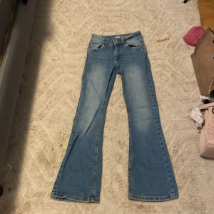 Blå bootcut jeans från Denim Day - Snygga blå bootcut jeans från Denim Day i storlek 152. Jeansen har klassisk femficksdesign, silverfärgade nitar på bakfickorna och ljus tvätt. Materialet är jeans och passformen är loose med breda ben. Perfekt för dig som gillar lite extra detaljer på dina jeans.