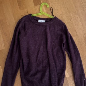 Mörklila stickad tröja från Vila - Säljer en mörklila stickad tröja från Vila med rund hals och långa ärmar. Tröjan har ribbade muddar vid ärmslut och nederkant, perfekt för dig som gillar enkel och stilren design. Den är lite nopprig men det går att fixa 