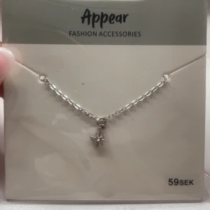 Silverfärgat halsband med stjärnhänge - Snyggt halsband från Appear med en tunn silverfärgad kedja och ett litet stjärnformat hänge med en glittrande sten i mitten. Perfekt för dig som gillar minimalistiska smycken med en touch av bling.