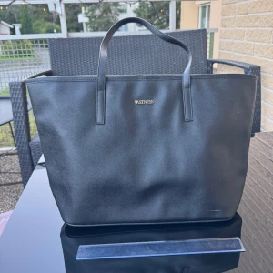 Ny Svart handväska / bag  - Helt ny stor och stilren svart hand /axel väska med två rejäla handtag. Väskan har en enkel, fyrkantig form och är tillverkad i slätt syntetmaterial. Insidan är ljusbeige med flera fack och dragkedja för smidig organisering. Perfekt för dig som vill ha plats för allt.