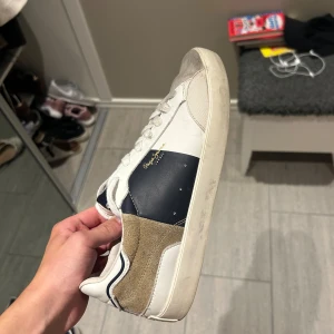 Pepe Jeans vita och blå sneakers - Snygga sneakers från Pepe Jeans i vitt och marinblått med beige mockadetaljer på hälen. Skorna är stolen 41, men skulle säga att de passar 42 också. Inte använda mycket hursomhelst lite smutsiga. Väldigt gott skick. Lådan följer med. Skriv vid funderingar. Pris ej hugget i sten!🪨 