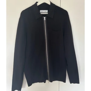 Svart kofta med dragkedja från Samsoe - Svart kofta från Samsoe Samsoe med hel dragkedja framtill och klassisk krage. Tröjan har en enkel bröstficka och är långärmad. Perfekt för dig som gillar stilrena och minimalistiska plagg med snygga detaljer.