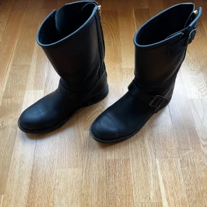 Svarta boots med spänne - Säljer ett par svarta boots i skinn med rund tå och platt sula. De har snygga spänndetaljer på sidan och en robust look som passar till jeans eller kjol. Perfekta för dig som gillar stilrena och tidlösa skor med lite edge. Använda 1/2 gånger. Köpta för 3199kr. (Orginalkartong medföljer)