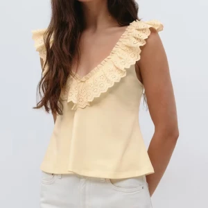 Gul linnetopp med volang - Supersöt ljusgul linnetopp med breda volangdetaljer runt v-ringningen och axlarna. Toppen är ärmlös och har en lätt utsvängd passform som ger en skön och luftig känsla. Perfekt för soliga dagar och sommarhäng.