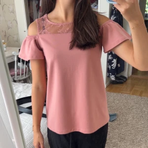 Rosa blus med spets från Lindex - Supersöt rosa blus från Lindex med offshoulder och korta ärmar. Överdelen har transparent spets med blommigt mönster! Perfekt till sommaren, inga tecken på användning 