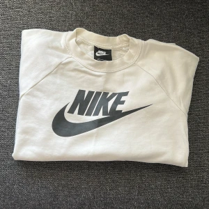 Vit sweatshirt från Nike med logga - Säljer en fräsch vit sweatshirt från Nike med stor svart logga på bröstet. Tröjan har rund hals och är tillverkad i mjuk bomull.