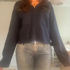 Mörkblå tunn höstjacka med dragkedja - Snygg mörkblå jacka med dragkedja framtill och två bröstfickor. Modellen är croppad och har långa ärmar, perfekt att slänga på sig över en t-shirt. Materialet känns mjukt och skönt mot huden. Enkel och stilren design som funkar till jeans eller kjol.