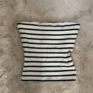 Randig offshoulder topp från BikBok - Säljer en vit och svart randig offshoulder topp från BikBok i storlek S. Toppens material är mjuk bomull och den har en slim passform som sitter snyggt. Perfekt för dig som gillar klassisk stil med en modern twist.