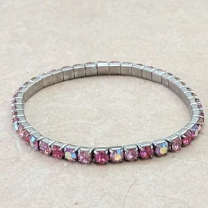 Glittrigt rosa armband med stenar - Snyggt elastiskt armband i silverfärgad metall med glittrande rosa stenar runt hela bandet. Stenarna har olika nyanser av rosa och vissa har en skimrande effekt som fångar ljuset. Perfekt för dig som vill ha lite extra bling i din stil.