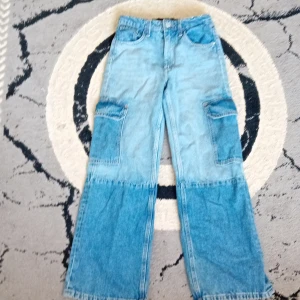 Två olika blå nyanser  - Unika cargobyxor i patchwork-stil med två olika blå denimnyanser. Vida ben, stora cargofickor på sidorna och klassiska jeansfickor fram och bak. Snygg kontrast mellan ljus och mörk denim, perfekt för dig som vill sticka ut. Materialet är 100% bomullsjeans.