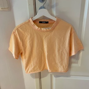 Ljus orange croppad topp från Bik Bok - Fräsch ljus orange croppad topp från Bik Bok i storlek S. T-shirten har rund hals, korta ärmar och är gjord i mjuk bomull. Perfekt för dig som gillar en chill och enkel stil med lite edge tack vare den croppade passformen.