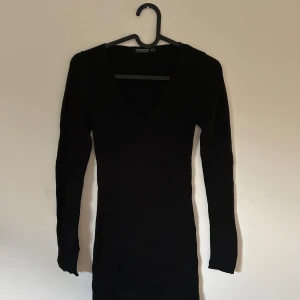 Svart ribbad klänning, Stradivarius - Svart ribbad knälång klänning från Stradivarius med lång ärm och v-ringning. Klänningen är figurnära med ett stretchigt tyg. Den är stilren med enkel design som är användbar både under sommar och vinter.