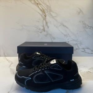 DiorB30 - Snygga svarta sneakers från  med reflekterande silverdetaljer och tydlig logga på sidan och plösen. Skorna har en chunky sula och är tillverkade i mesh och syntetmaterial för en modern och sportig look. Perfekta för dig som vill sticka ut med exklusiva sneakers.
