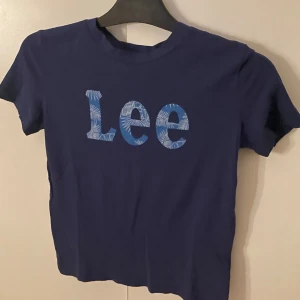 Mörkblå Lee t-shirt med tryck - Snygg mörkblå t-shirt från Lee med stort tryck på bröstet i blått och vitt med mönstrade bokstäver. Modellen är kortärmad och har en klassisk rund hals. Perfekt för dig som gillar streetwear och vill ha en enkel men cool look.