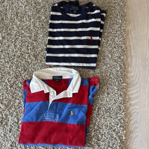 Randiga långärmade pikétröjor Polo Ralph Lauren - Två långärmade pikétröjor från Polo Ralph Lauren. Ena är marinblå och vit med smala ränder och röd logga på bröstet, den andra har breda ränder i rött och blått med vit krage och gul logga. Båda är i mjuk bomull och har klassisk passform.