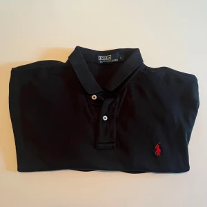 Svart pikétröja från Ralph Lauren - Stilren Svart pikétröja från Polo Ralph Lauren i storlek L men kan passa M också. Varan är äkta och använd bara ett fåtal gånger. Kan mötas i Sthlm eller frakta 🚚 