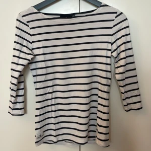 Randig topp från Cross Sportswear - Snygg vit och marinblå randig topp från Cross Sportswear i storlek 36. Modellen har trekvartsärm och är tillverkad i mjuk bomull. Perfekt för dig som gillar en klassisk och stilren look.